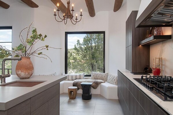 A modern kitchen with a built-in stove, a large window with a view, and a seating area with a plant.