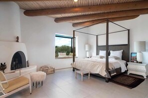 A bedroom with a four-poster bed, a fireplace, a window with a view, and a white nightstand.