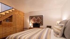 A bedroom with a bed, a TV, a wooden wardrobe, and a staircase.