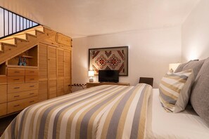 Un dormitorio con una cama, televisor, armario de madera y una escalera.