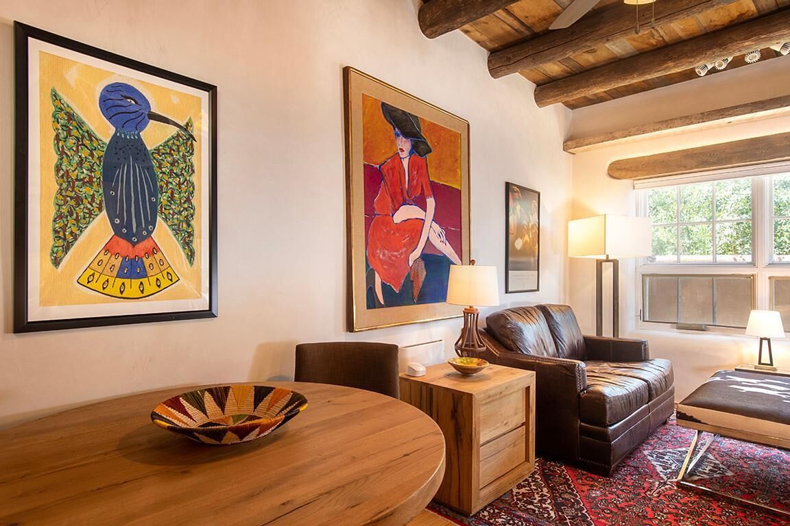 A living room with a wooden dining table, a leather sofa, and two framed paintings on the wall.