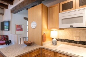 A kitchen with wooden cabinets, a microwave, a clock, a bowl, and a lamp.