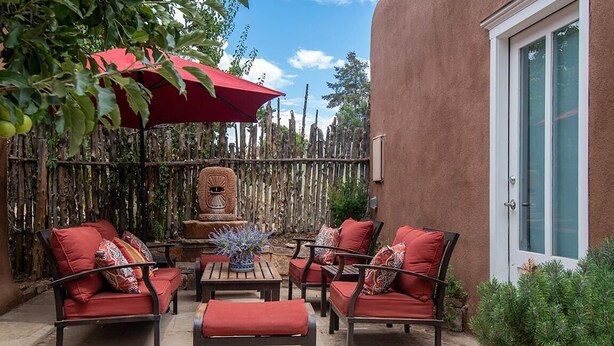 An outdoor patio with a red umbrella, wicker furniture, and a decorative fountain.