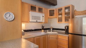A kitchen with wooden cabinets, a microwave, a stainless steel refrigerator, and a clock on the wall.