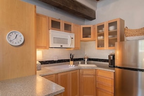 Una cocina con armarios de madera, microondas, refrigerador de acero inoxidable y un reloj en la pared.