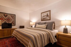 A hotel room with a bed, two bedside tables, a TV, a painting, and a patterned rug.