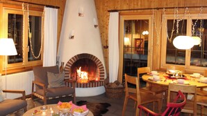 A cozy room with a fireplace, wooden walls, a dining table set for two, and a comfortable seating area. - Cozy family apartment with stove, gallery and magnificent alpine view (Adelboden)