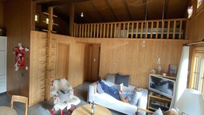 A cozy room with a wooden ceiling, a sofa, a dining table, and a TV. - Cozy family apartment with stove, gallery and magnificent alpine view (Adelboden)