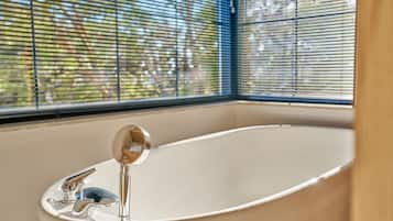 Un baño con bañera, grifo y ventana con persianas.