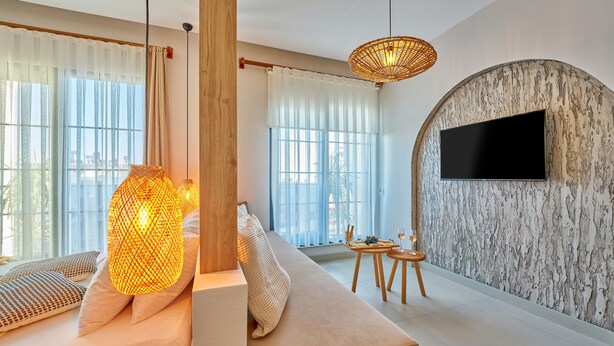 Una sala de estar moderna con un sofá, un televisor montado en una pared con textura, y un comedor con una mesa pequeña y sillas.