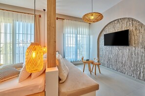 A modern living room with a sofa, a TV mounted on a textured wall, and a dining area with a small table and chairs. - Lilium Boutique Hotel (Antalya)