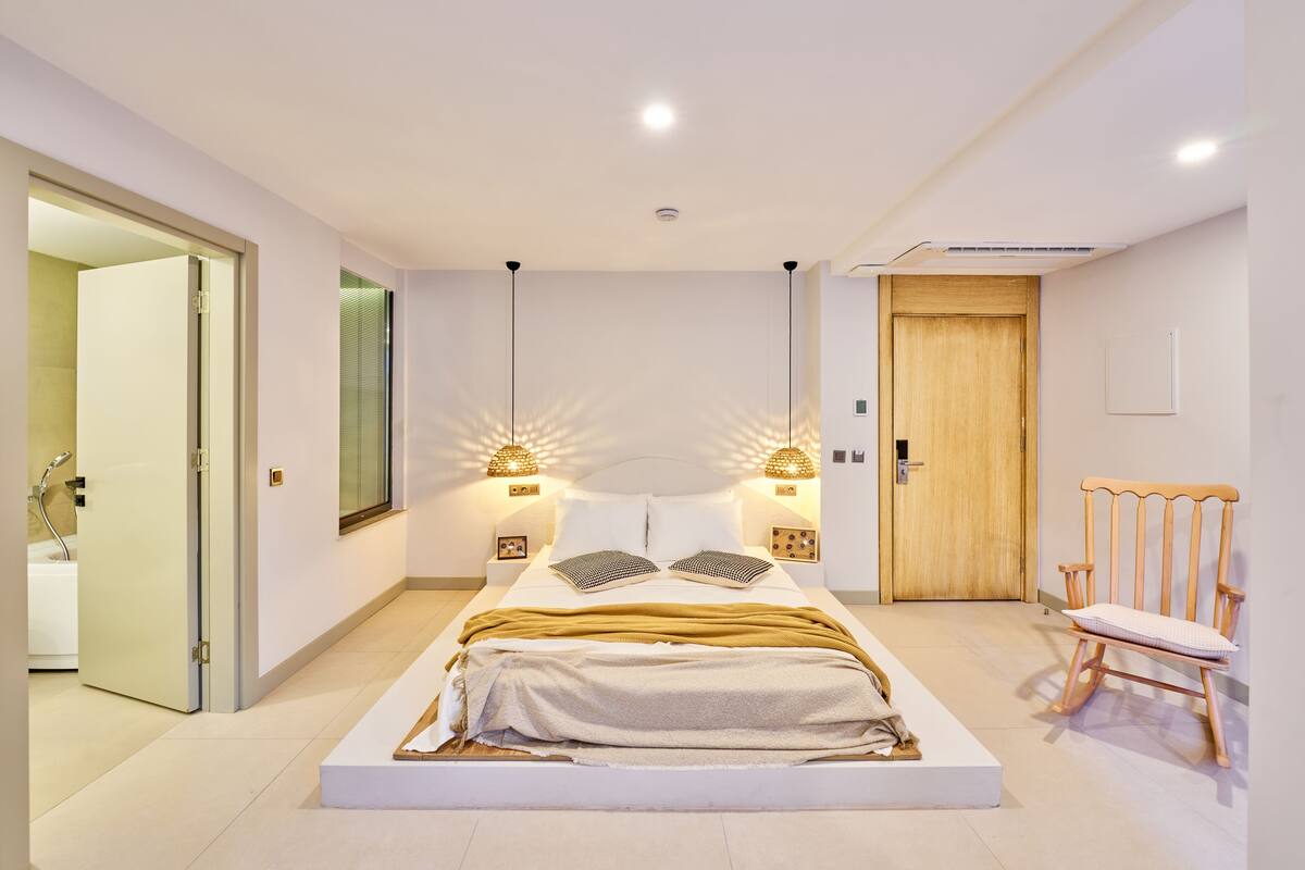 Een moderne slaapkamer met een groot bed, nachtlampjes, een houten deur en een stoel.