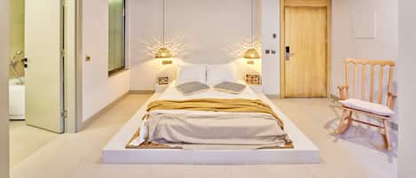 Un dormitorio moderno con una cama grande, lámparas de noche, una puerta de madera y una silla.