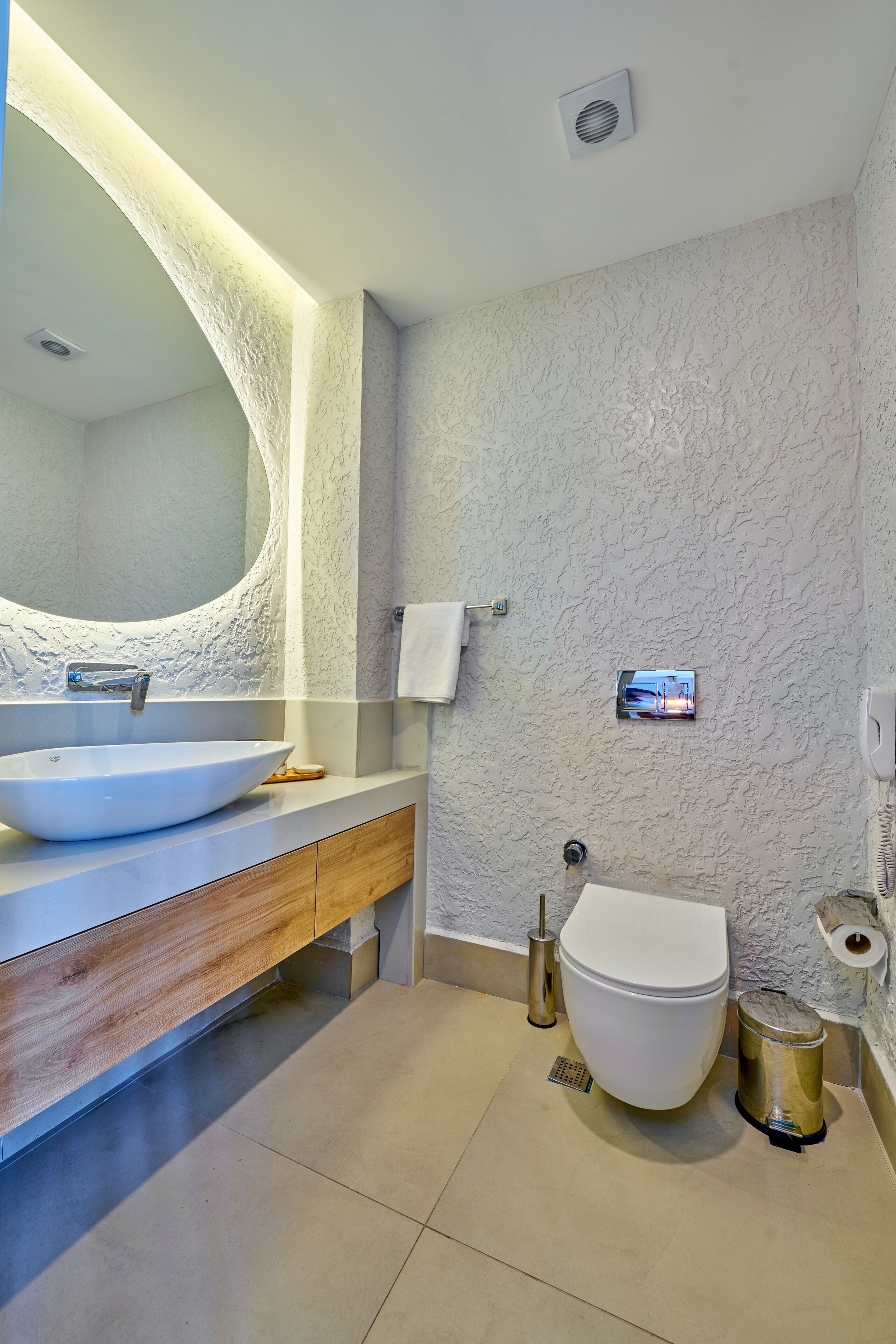 Un baño moderno con un espejo ovalado grande, un lavamanos blanco y un inodoro.