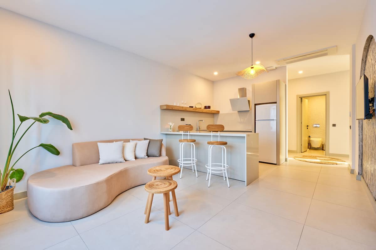 Een moderne woonkamer met een gebogen bank, twee rieten krukjes, en een keuken met een bar.