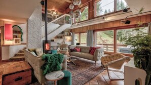 A spacious living room with a fireplace, a staircase, and large windows offering a view of the outdoors. - Large chalet, peaceful setting ideal for Cham adventures, Flégère & Grand Montet (Chamonix-Mont-Blanc)