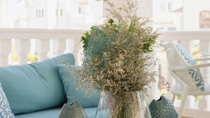 Une table à plateau en verre, ornée d’un vase de fleurs séchées, d’une sculpture d’oiseau décorative et d’un vase texturé. Un canapé de couleur turquoise, agrémenté de coussins à motifs, se trouve à l’arrière-plan.