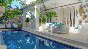 Un espace aménagé au bord de la piscine, avec une eau cristalline, des chaises longues blanches et un canapé en osier.