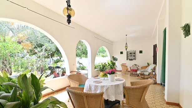 Un comedor con una mesa redonda, sillas de mimbre y vistas al exterior con vegetación.