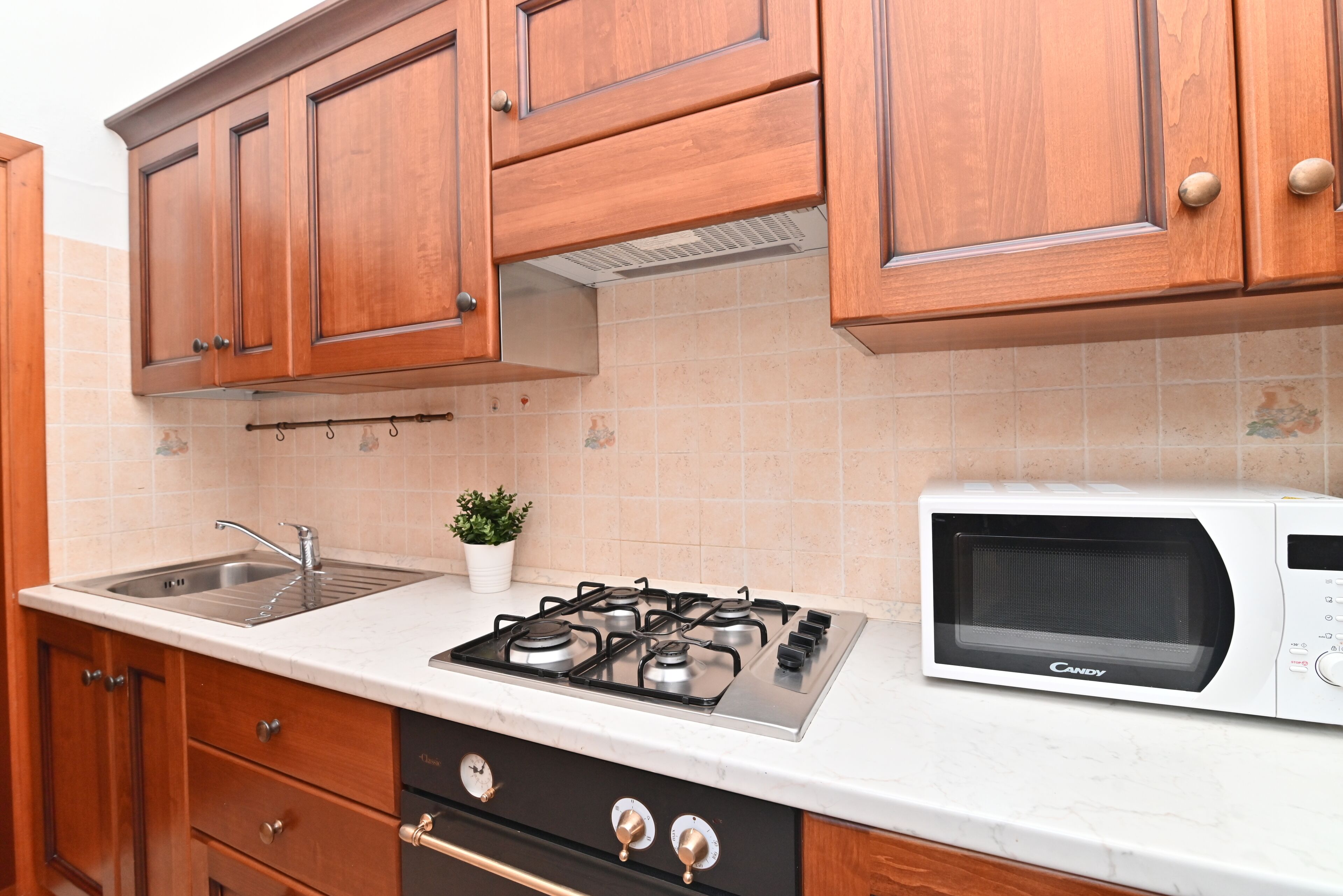 Una cocina con gabinetes de madera, un lavamanos de acero inoxidable, una estufa y un microondas.