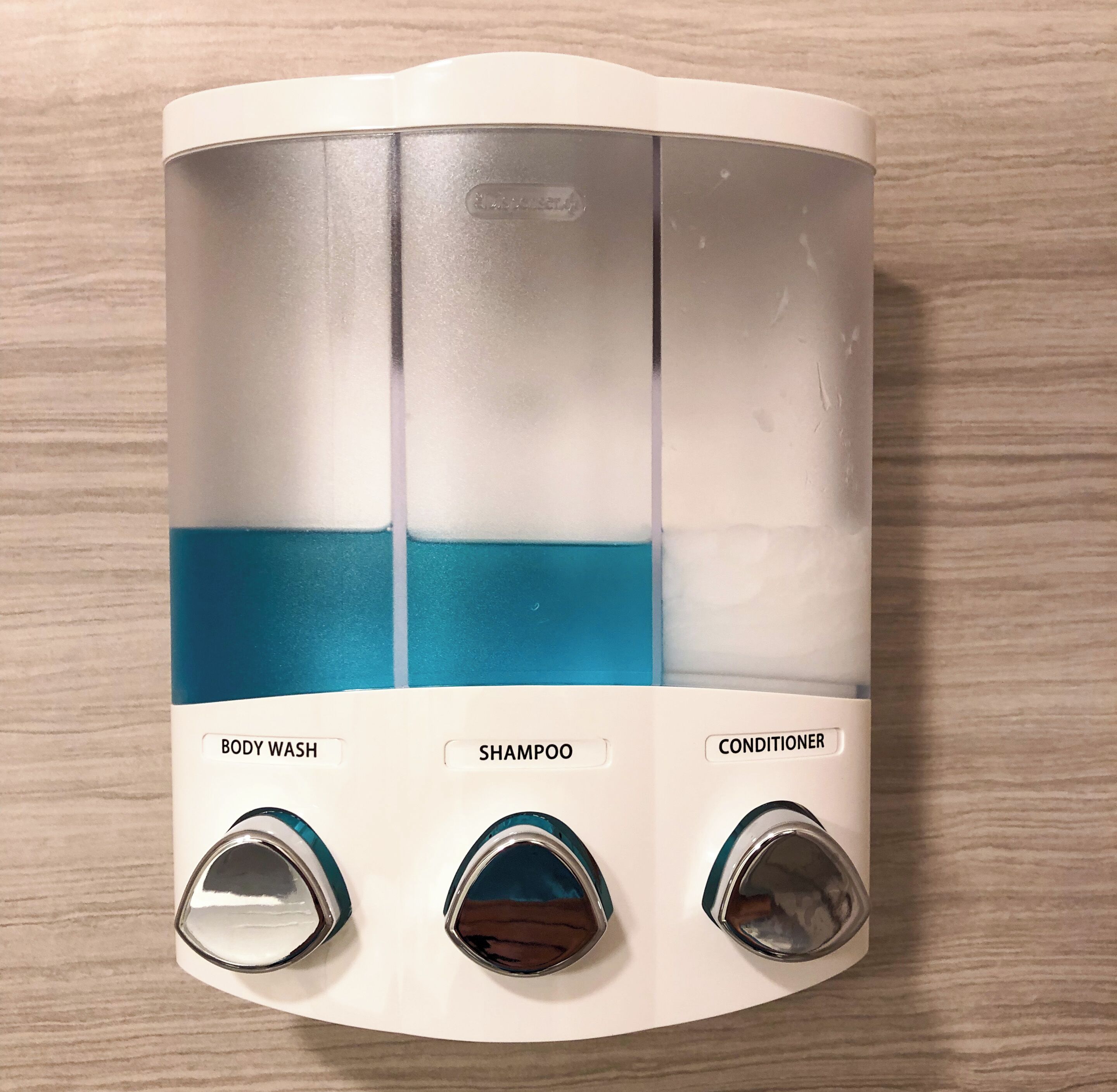 Un baño con dispensador blanco montado en la pared que contiene gel de ducha, champú y acondicionador.