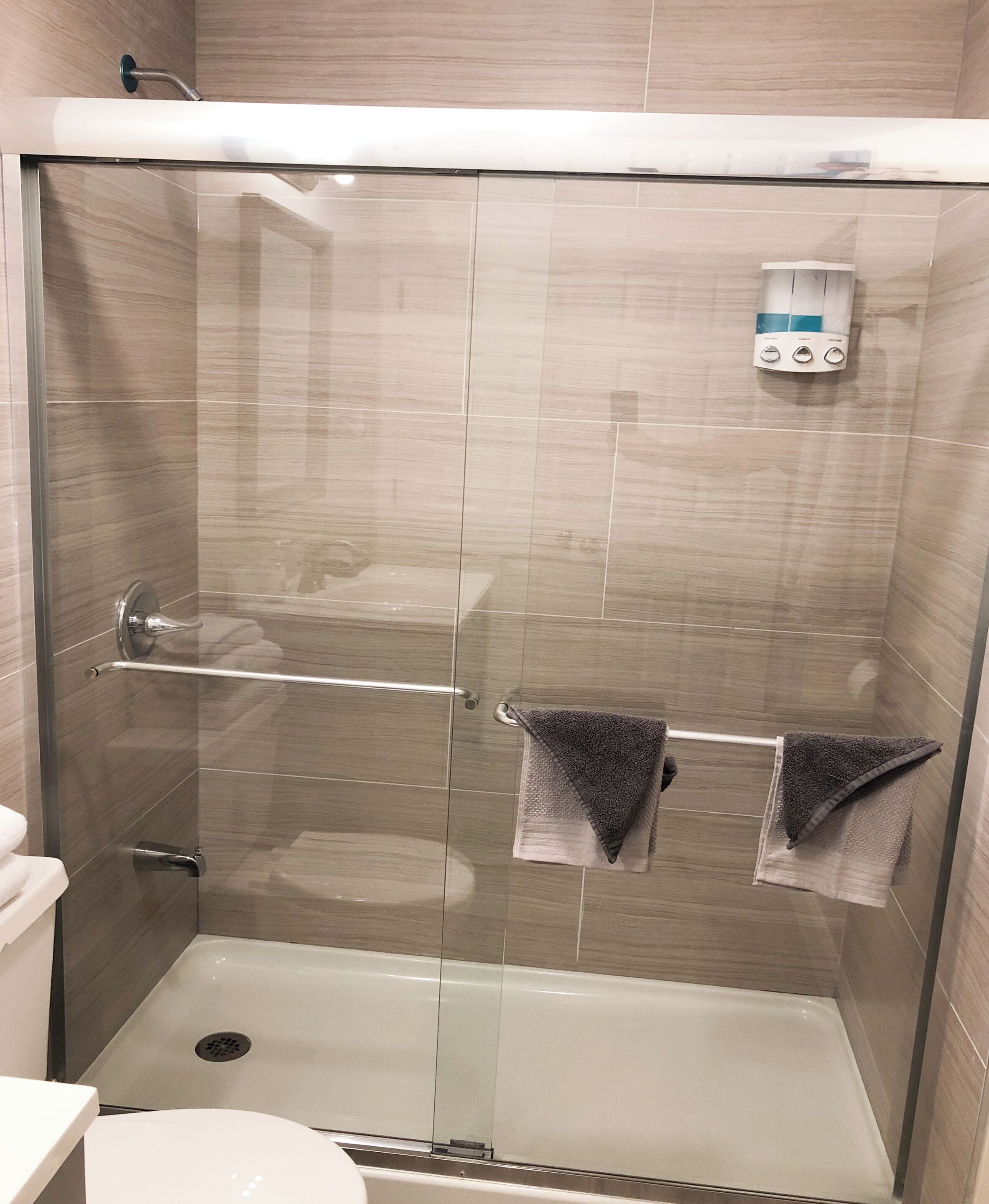 A glass-enclosed shower stall with a control panel, a towel rack, and a visible toilet.