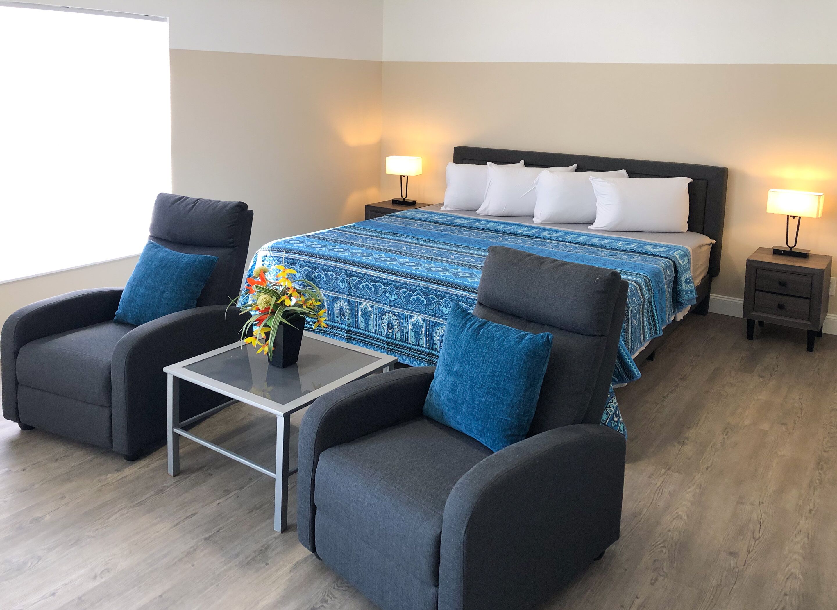 A hotel room with a bed, two armchairs, a small table with a vase of flowers, and two bedside lamps.