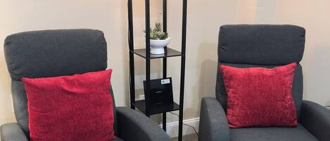 Two grey armchairs with red cushions and a black floor lamp with a white shade.