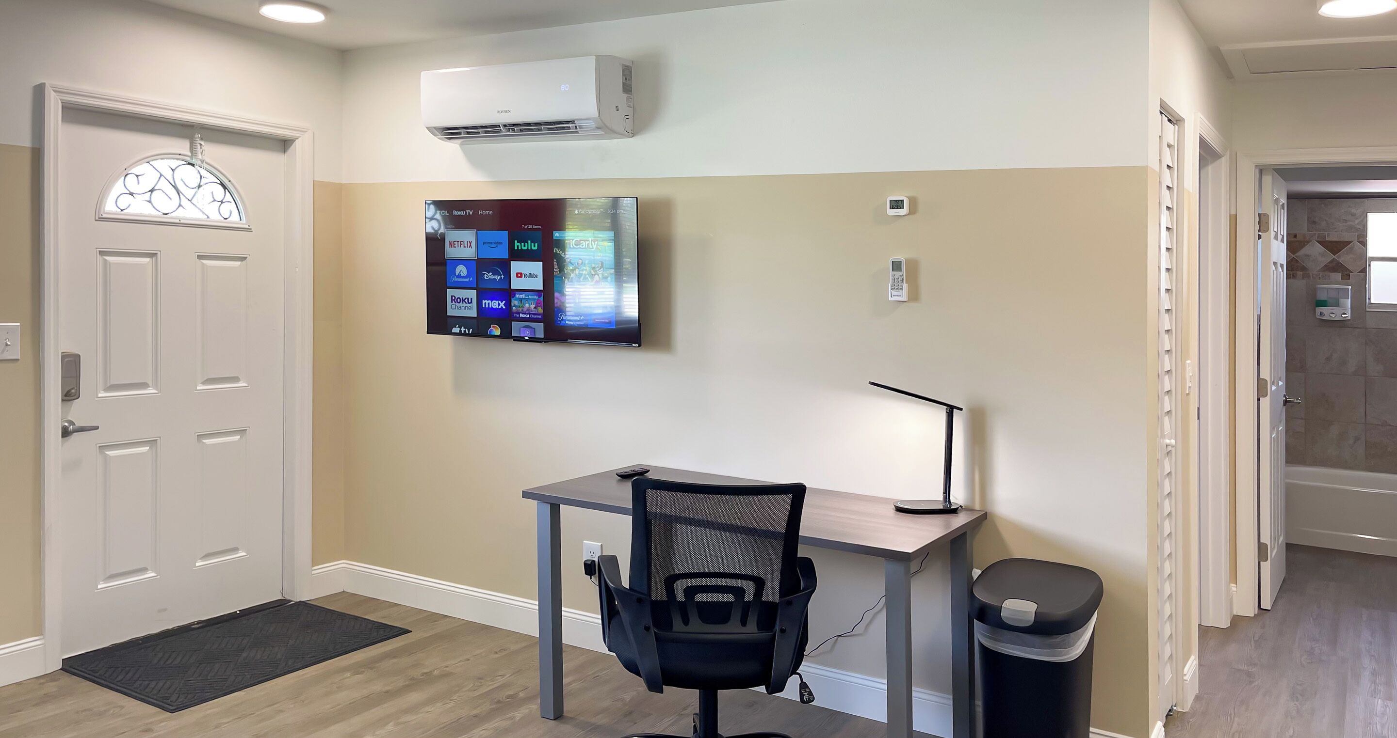 Un espacio de oficina moderno con un escritorio, una silla y un televisor de pantalla plana montado que muestra servicios de transmisión.