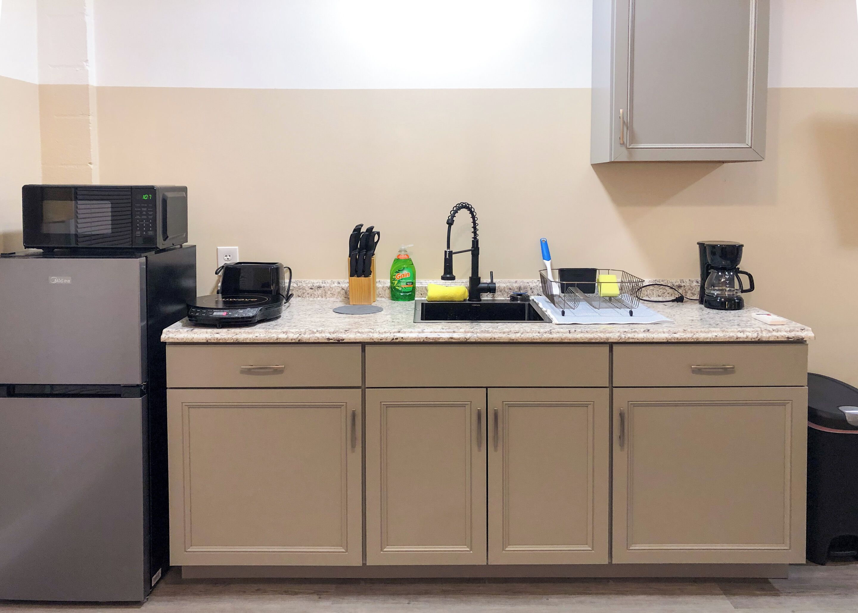 Eine kleine Küche mit Kühlschrank, Mikrowelle, Kaffeemaschine und Spüle mit Armatur.