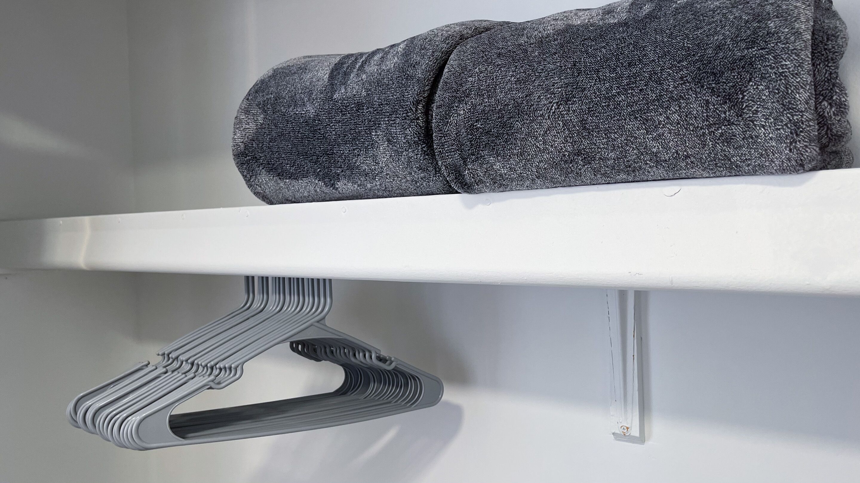A white shelf with a folded gray garment on top and a metal hanger below.