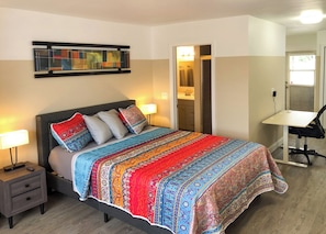 Cozy retreat with a large bed, nightstand, desk, and modern artwork.