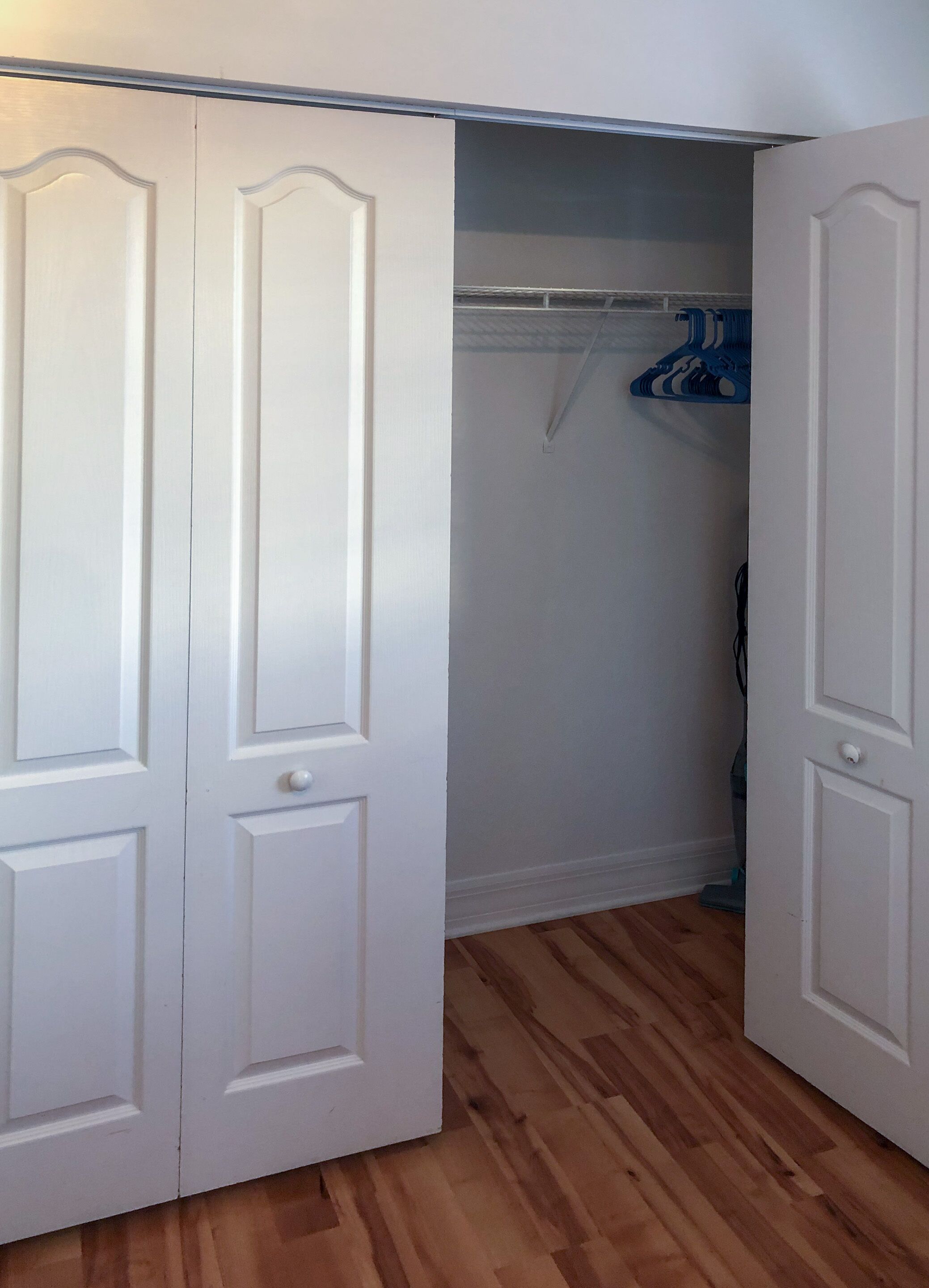 A closet with white doors and a wooden floor.