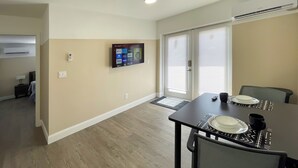 A dining area with a table set for two, a television mounted on the wall, and a sliding glass door leading to a balcony. - Lazy Cuckoo Inn (Fort Myers Beach)