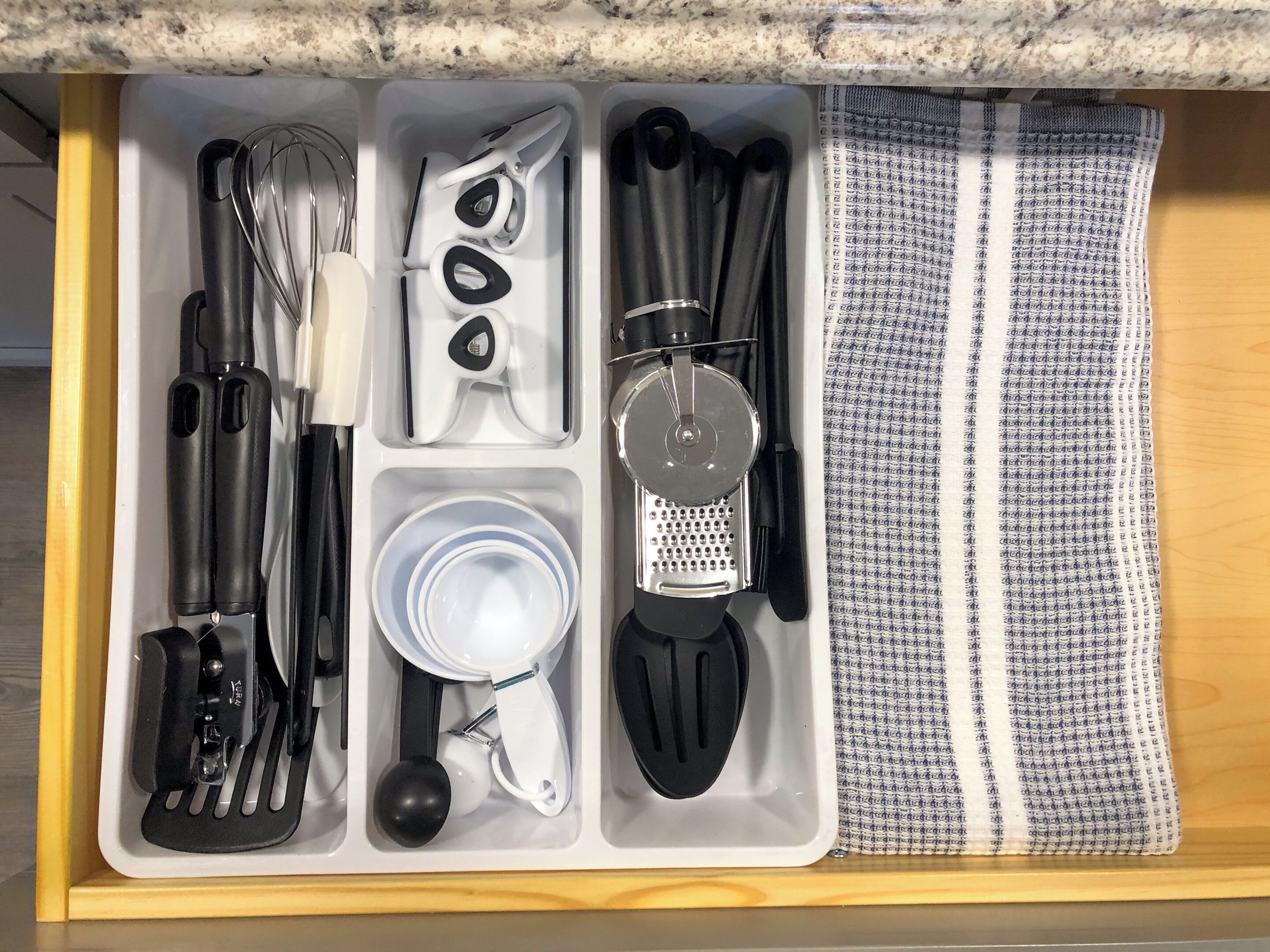 A kitchen drawer with utensils, including a whisk, scissors, a grater, and a cloth.
