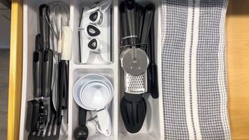 A kitchen drawer with utensils, including a whisk, scissors, a grater, and a cloth.