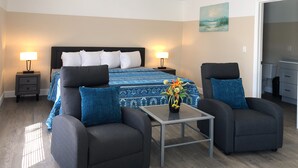 A modern bedroom with a bed, two bedside tables with lamps, a small table with a vase, two armchairs, and a painting on the wall. - Lazy Cuckoo Inn (Fort Myers Beach)