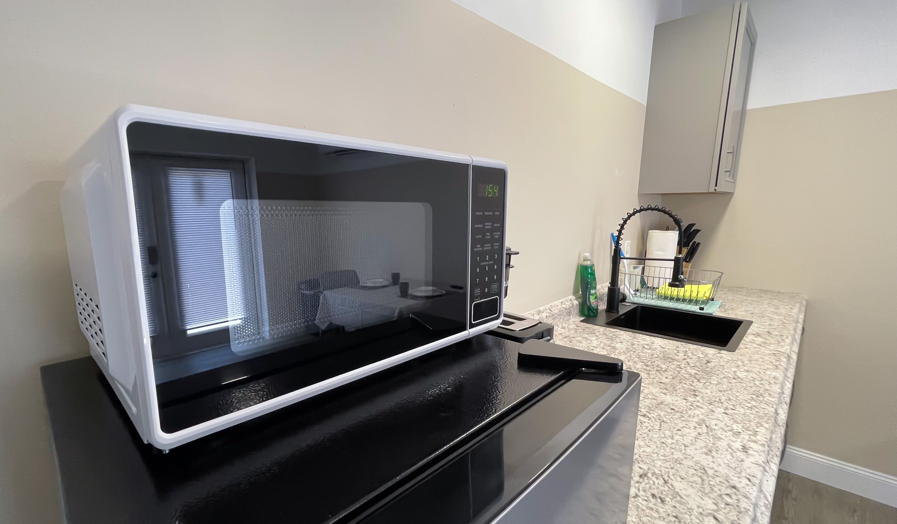 A kitchen with a microwave on a black countertop, a sink with a faucet, and a dish rack.