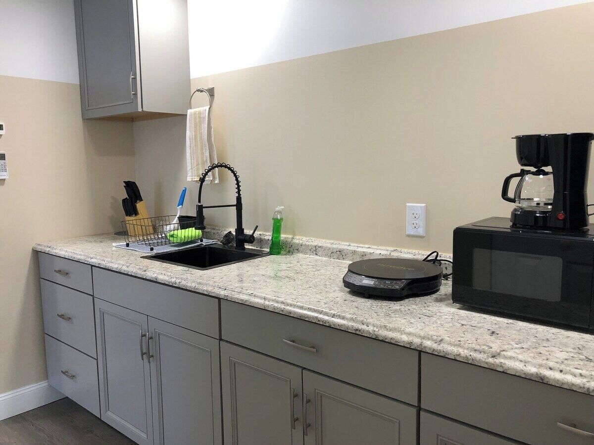 A kitchen with a granite countertop, a coffee maker, a microwave, and a dish rack.