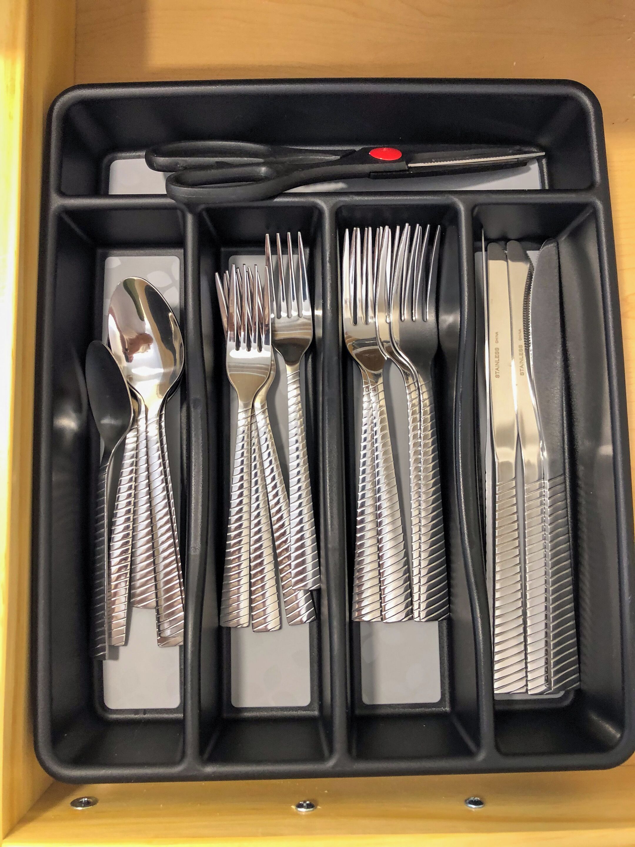 Une trousse noire avec des compartiments contenant un couteau, une fourchette, une cuillère et une paire de ciseaux.