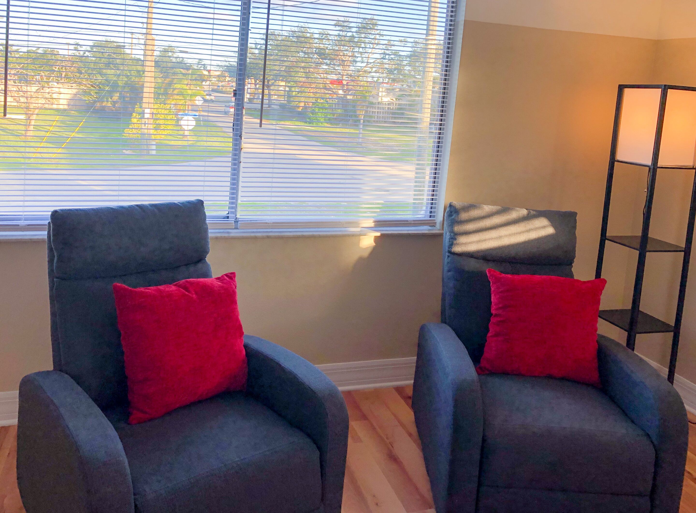 Two armchairs with red cushions in a room with a window overlooking a street.