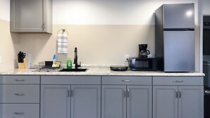 A modern kitchen with grey cabinets, a stainless steel refrigerator, a coffee maker, and a dish drying rack. - Lazy Cuckoo Inn (Fort Myers Beach)