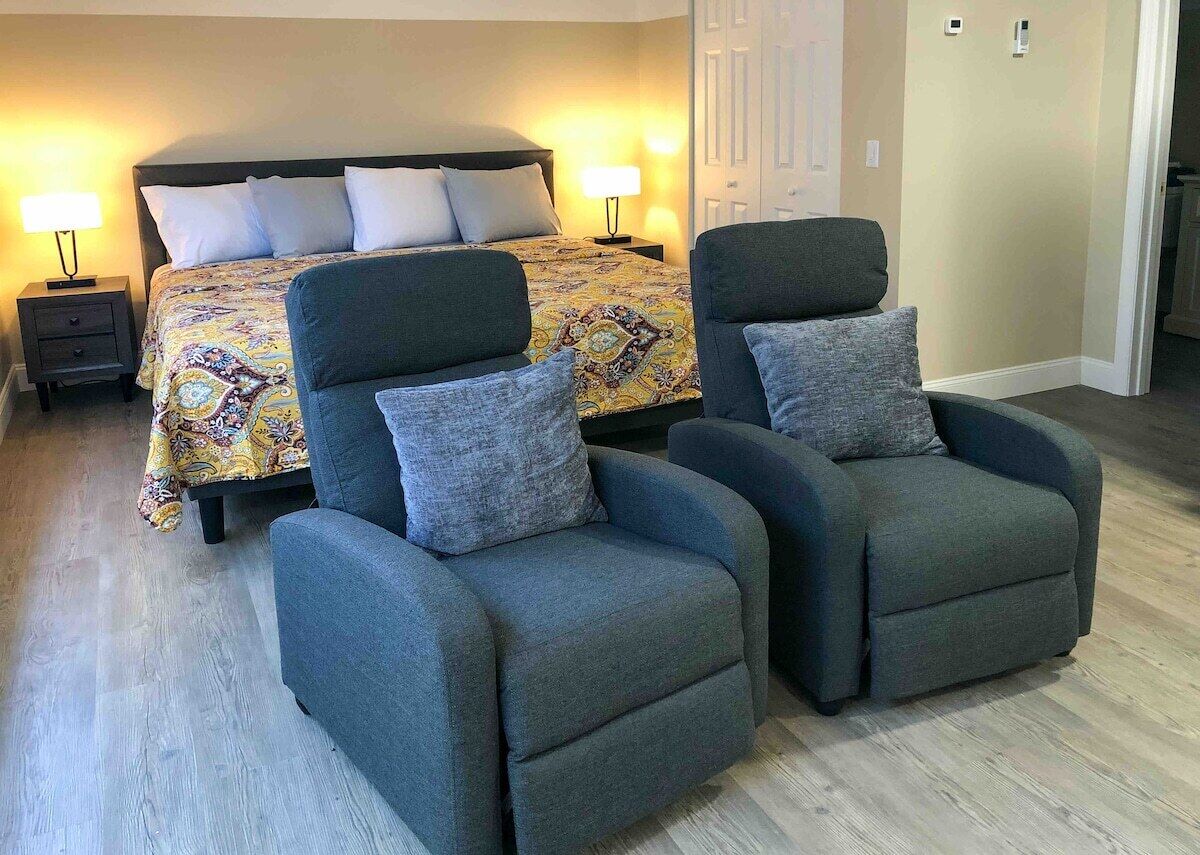Een slaapkamer met een bed, twee fauteuils, een nachtkastje en een bedlamp.