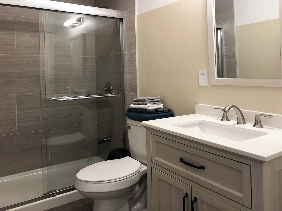 Un baño moderno con ducha de vidrio, inodoro blanco y lavamanos con espejo.