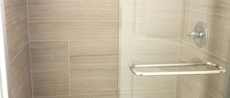 A glass-enclosed shower stall with a handheld showerhead, a towel rack, and a soap dispenser on the wall.