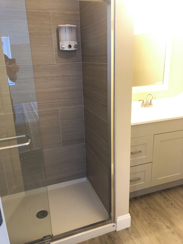Ducha con panel de control, puerta de vidrio y suelo de madera.