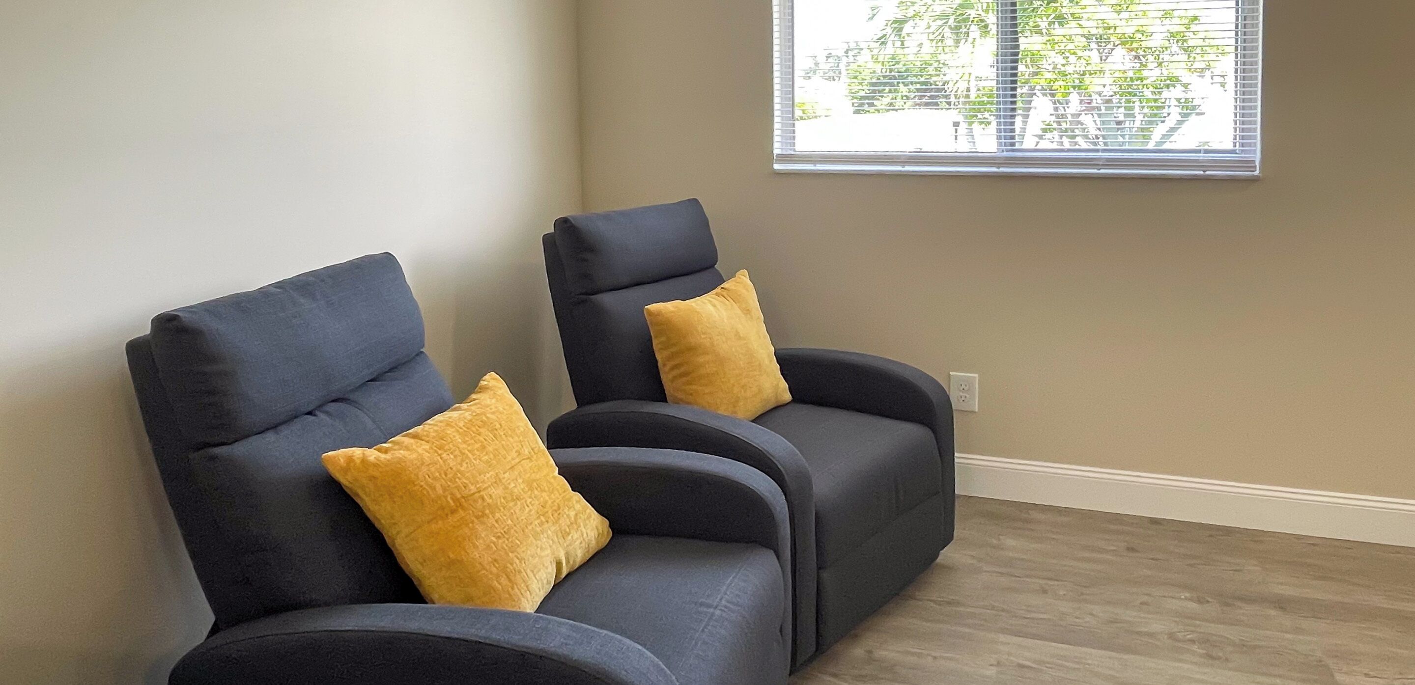 Dos sillones oscuros con cojines amarillos en una habitación con ventana y suelo de madera.