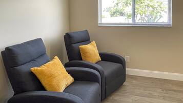 Dos sillones oscuros con cojines amarillos en una habitación con ventana y suelo de madera.