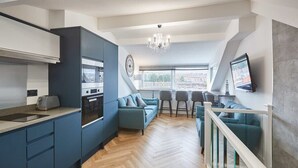 A modern kitchen with a built-in oven and microwave, a dining area with a sofa and chairs, and a view of the city through large windows. - Host & Stay | Wadsworth Cottage (Whitby)