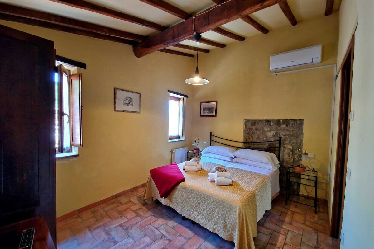A bedroom with a bed, a window, a radiator, and a stone wall.